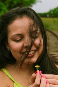 A smiling Hispanic woman joyfully holding a small flower in a lush green outdoor setting.