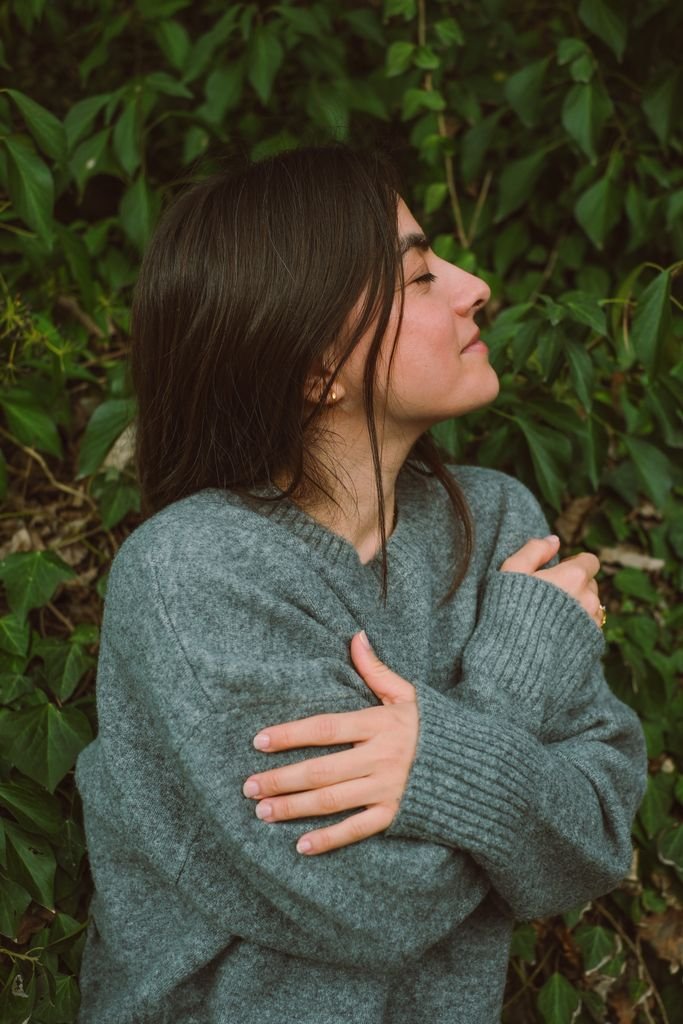 Peaceful portrait of a woman in a sweater, embracing nature with closed eyes and a serene smile.